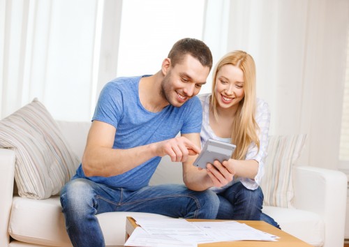 tax, finances, family, home and happiness concept - smiling couple with papers and calculator at home